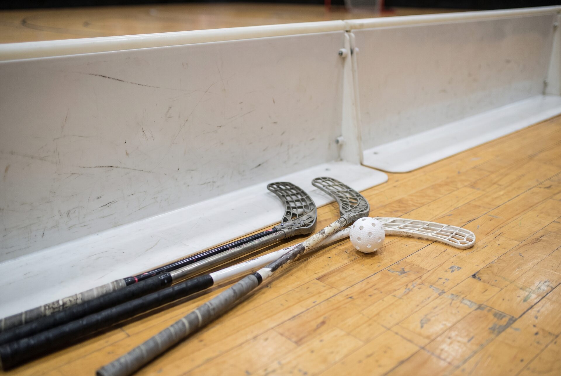Unihockeystöcke und ein Ball auf dem Hallenboden neben der Bande