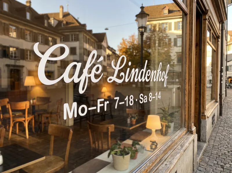 Weisser Schriftzug «Café Lindenhof» mit Öffnungszeiten als Klebeschrift auf dem Schaufenster eines Cafés in einer Altstadtgasse